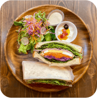 写真:木のお皿にサラダやサンドイッチやヨーグルトがのっています