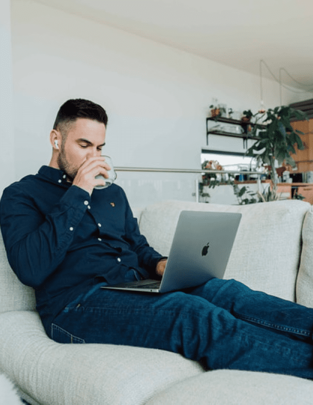 画像：グレーのソファーの上でパソコンを足の上に載せくつろぐ男性